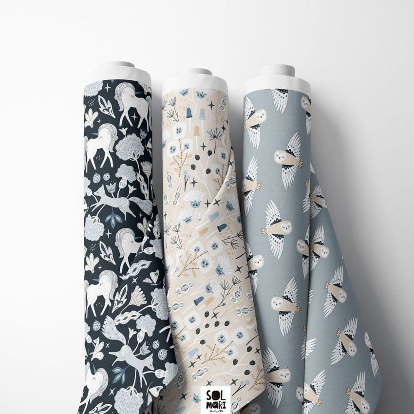 Fabric rolls mockup showing three upright rolls with whimsical animal and nature patterns in dark blue, beige, and light blue tones.