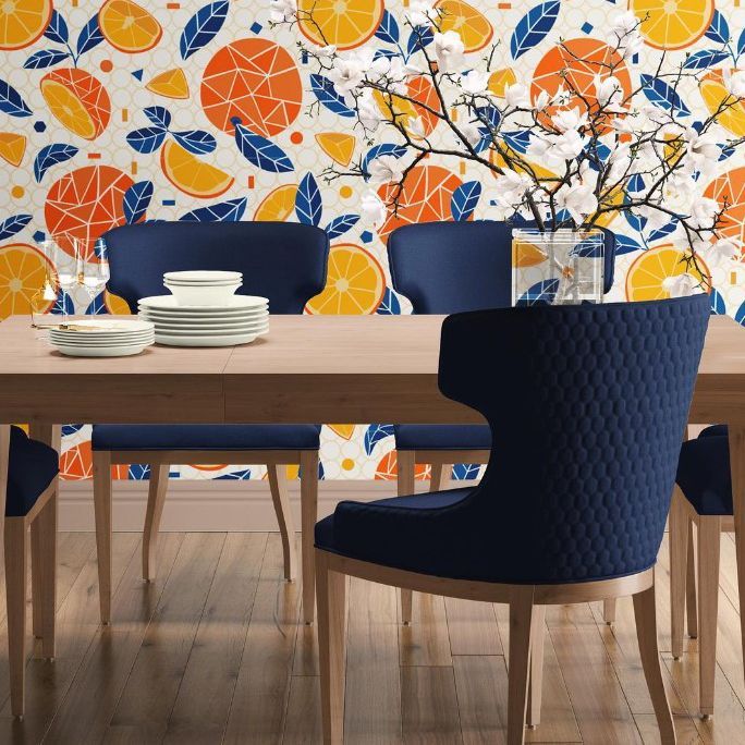 Dining room interior scene mockup featuring a wooden table set with white dishes, blue chairs, and a bold orange geometric wallpaper.