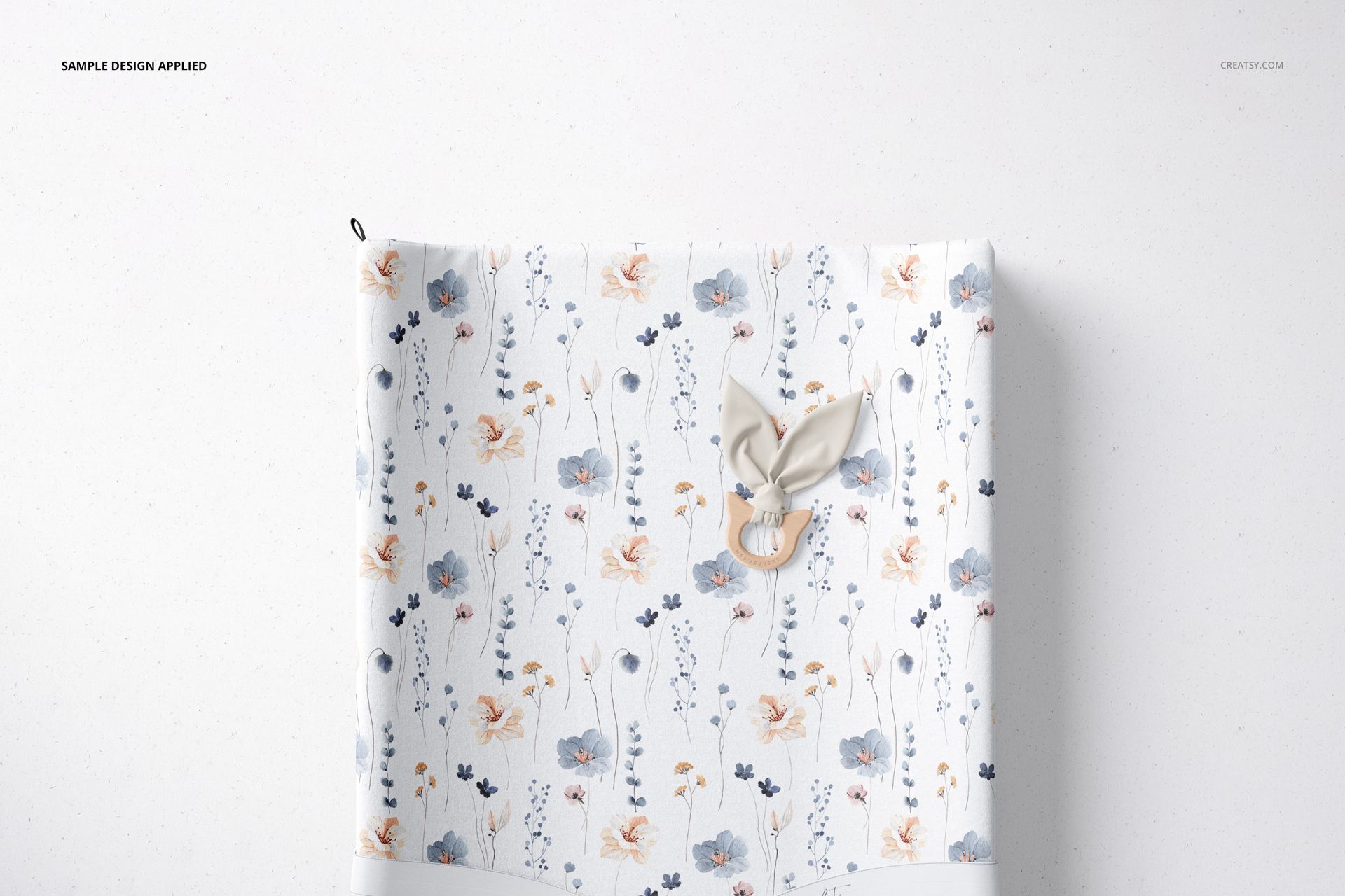 Top view of a changing pad mockup with a floral pattern in blue and peach tones, placed on a light surface.