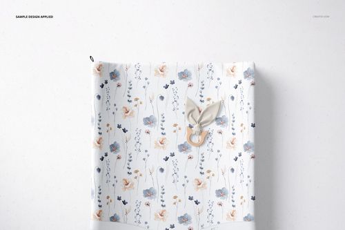 Top view of a changing pad mockup with a floral pattern in blue and peach tones, placed on a light surface.