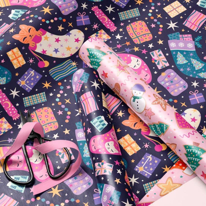 Gift wrapping paper mockup showing colorful Christmas patterns with stockings, presents, and stars on a flat surface.