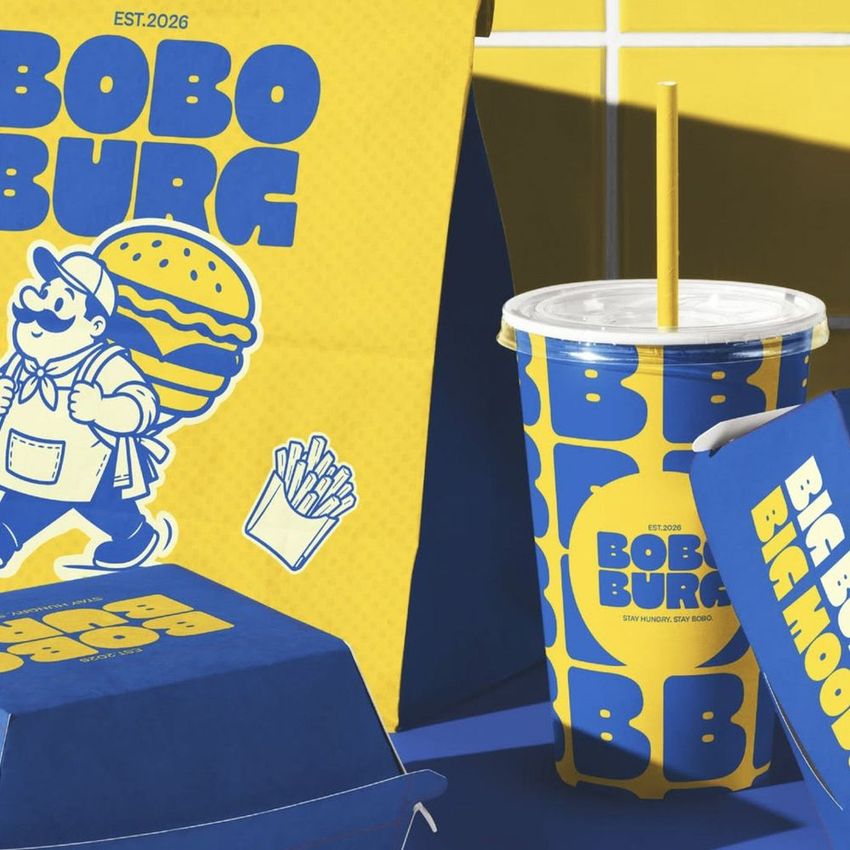 Burger packaging mockup featuring yellow and blue boxes, a drink cup, and illustrated fast food graphics on a blue surface.