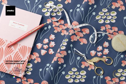 Cotton fabric with a floral pattern in pink and white on a blue background, displayed with a notebook, pen, scissors, and measuring tape in a top view scene.