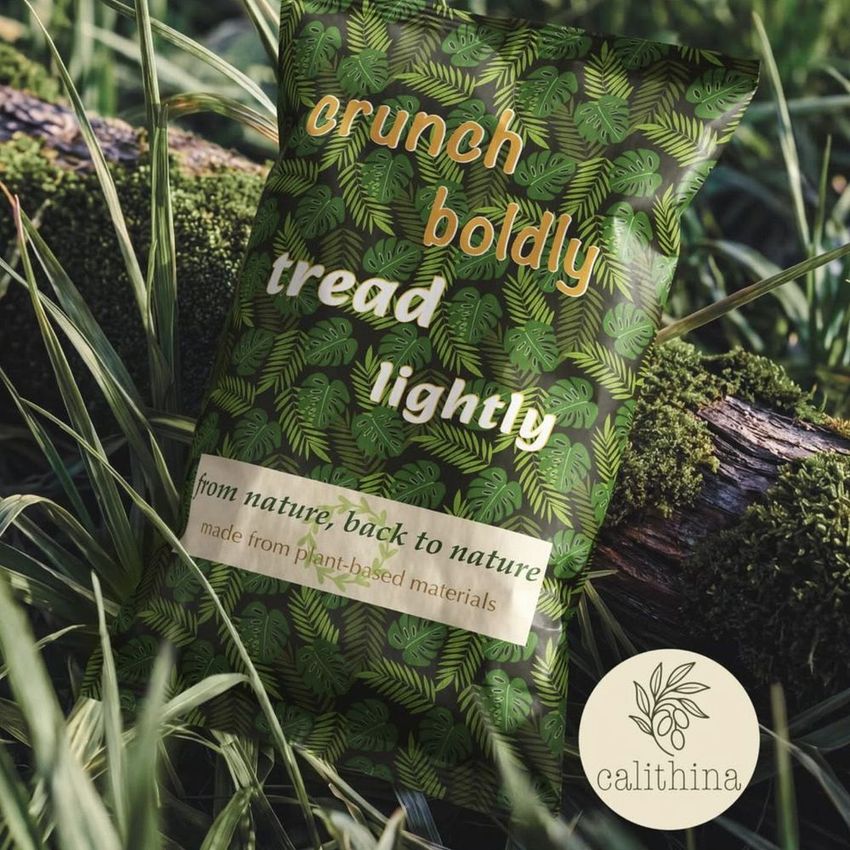 Paper chips bag mockup featuring a leafy green pattern, placed on a mossy log outdoors with grass and foliage around.