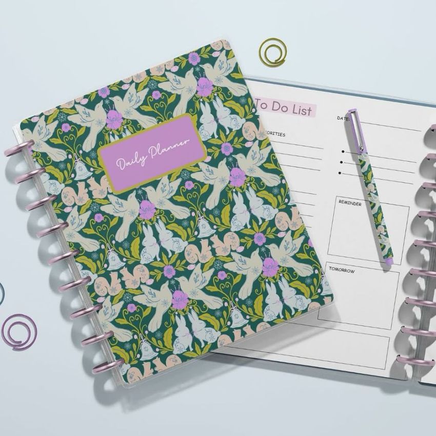 Top view of two spiral-bound planner mockups on a light surface, one closed with a colorful whimsical forest pattern, the other open to a to-do list page with a matching pen.