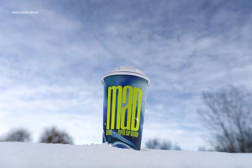 Winter-themed paper cup mockup featuring a bold graphic design, placed on snow with trees and sky in the background.