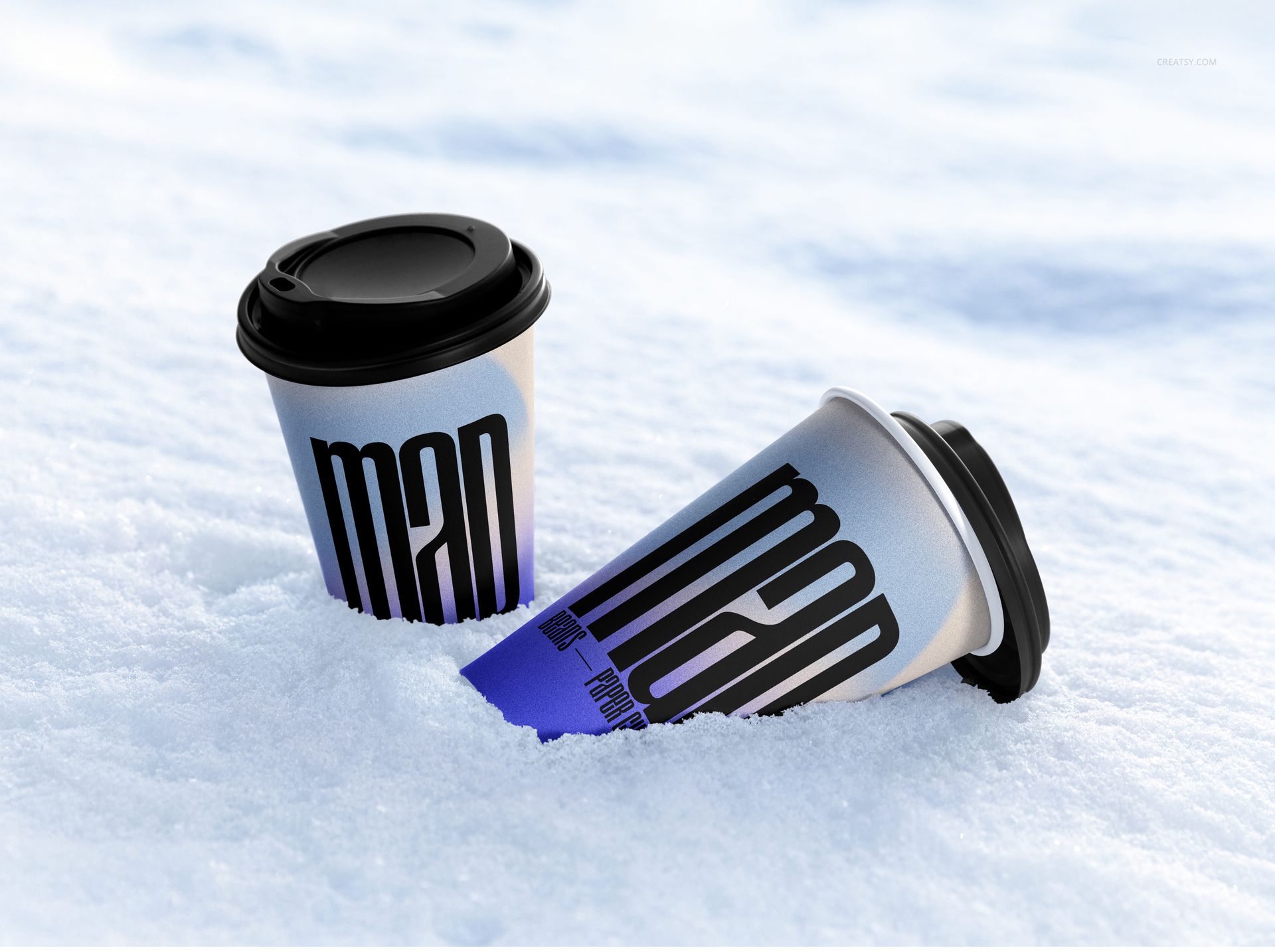 Winter-themed PSD mockup with two drinkware paper cups, black lids, and large text design resting in snowy surroundings.