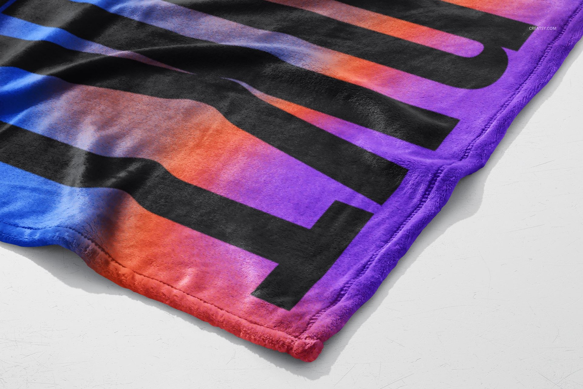 Close-up of a fleece blanket mockup featuring large black text over a vibrant gradient from red to purple on a white surface.