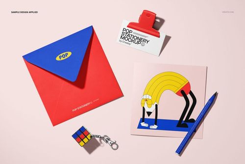 Stationery mockup featuring a square greeting card, colorful envelope, business card, pen, and Rubik's cube keychain arranged on a pale pink background.