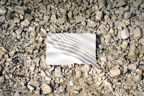 Rectangular business card mockup with blank white surface placed on rocky ground under clear water, top view.