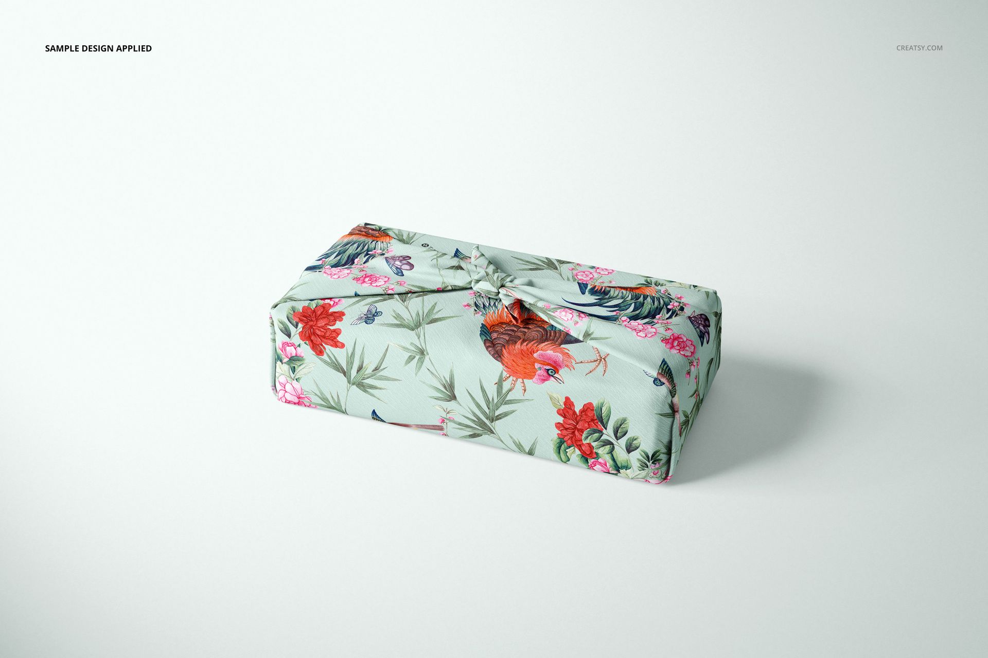 Furoshiki fabric wrap mockup featuring a pastel base with vibrant flowers and roosters, shown in a studio setting.
