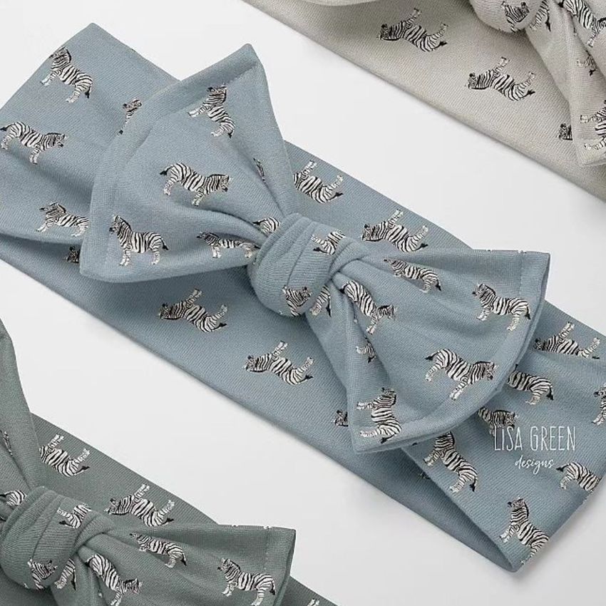 Kids adjustable bow tie style headband mockup featuring a blue fabric with a repeating zebra print pattern, shown from above.