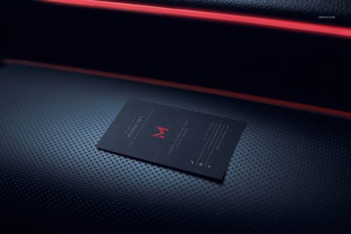 Single black business card mockup placed on a perforated car interior panel with red trim, close-up perspective.