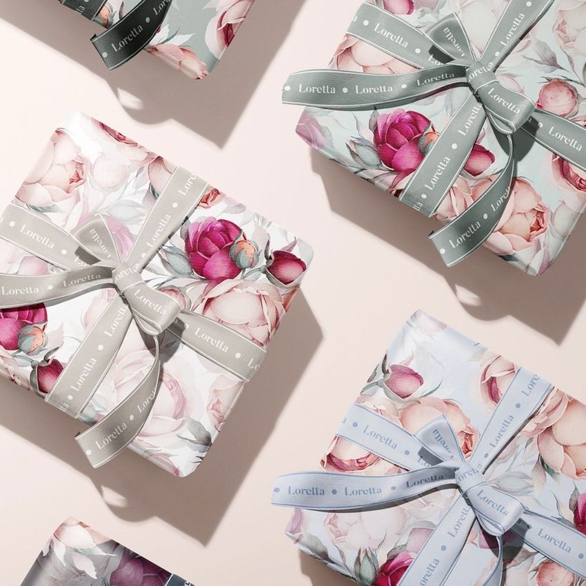 Gift box wrapping paper mockup featuring several boxes wrapped in floral paper with pastel ribbons, viewed from above on a light surface.