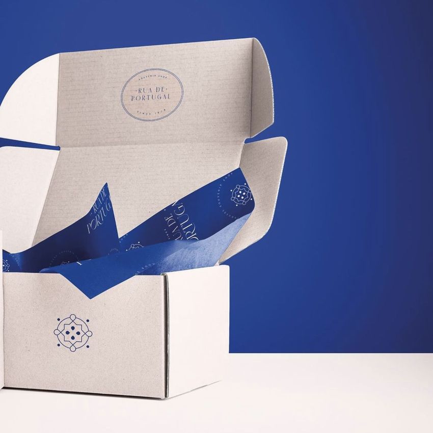 Mailing box mockup with blue patterned tissue paper inside, shown open on a white surface against a solid blue background.
