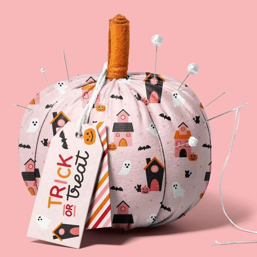Fabric pumpkin mockup with a pink Halloween-themed pattern, sewing pins, and a tag reading 'Trick or Treat' on a pink background.