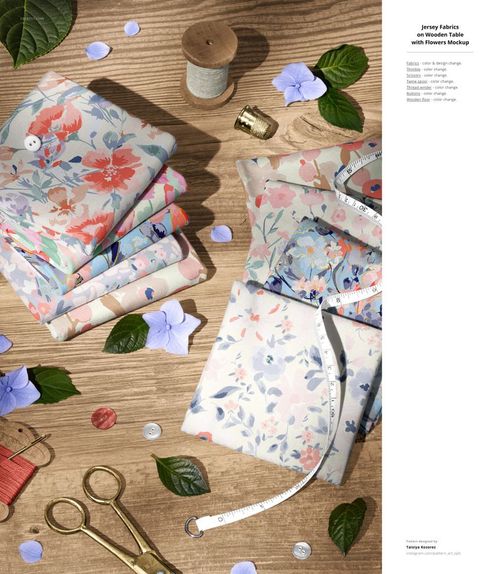 Jersey fabric mockup featuring layered floral textiles, scissors, thread, buttons, and green leaves on wood.