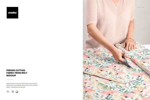 Person using scissors to cut floral patterned fabric from a bolt, viewed from above in a fabric mockup scene.