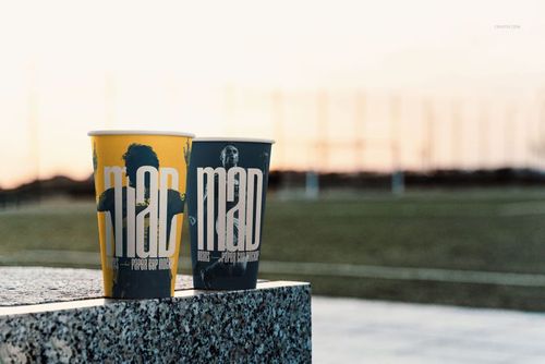 Mockup of drinkware showing two paper cups with contrasting designs, set against an open outdoor sports background.