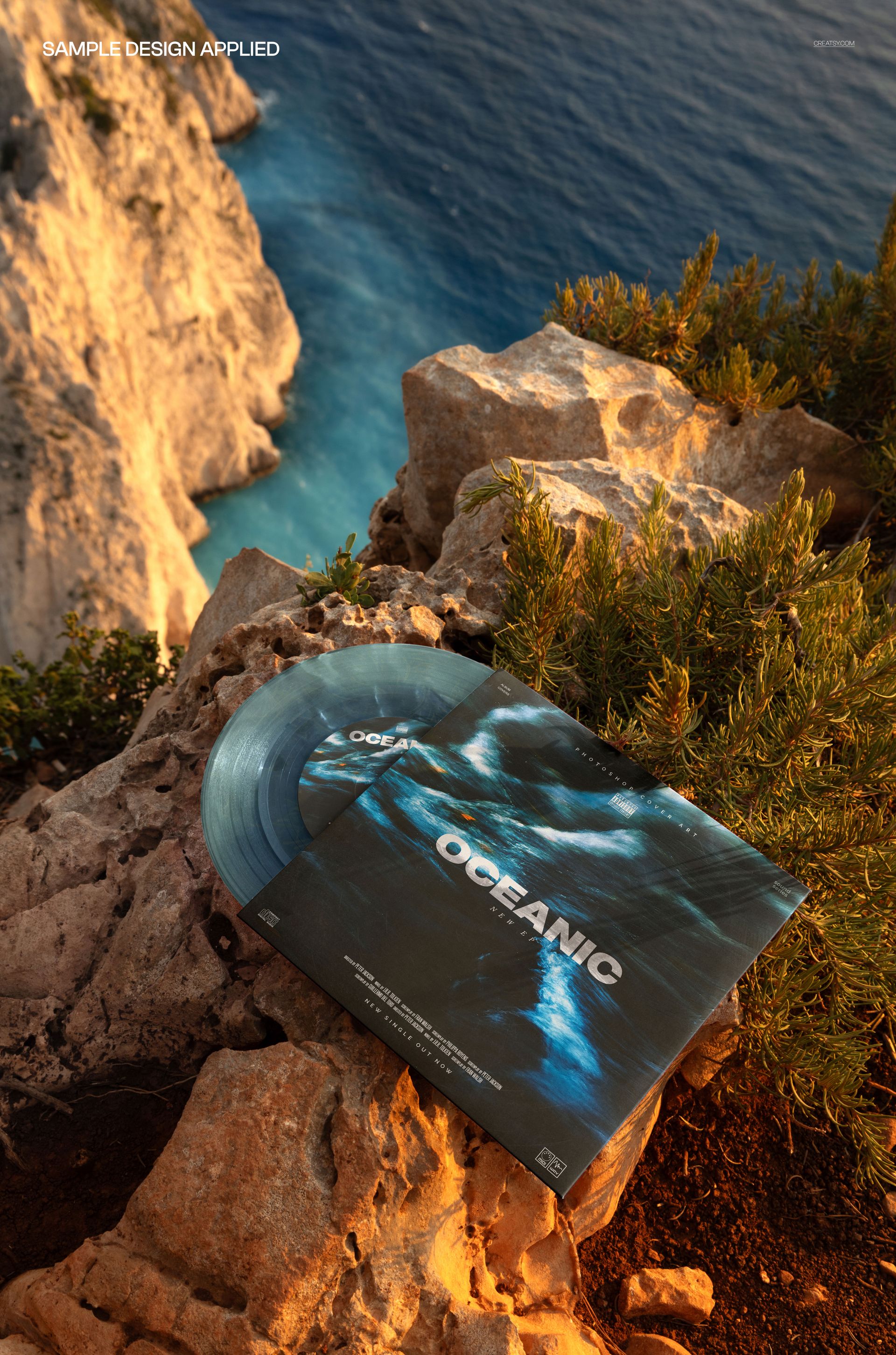 Top view of a 7 inch translucent vinyl record and cover mockup placed on rugged cliffside above blue water.