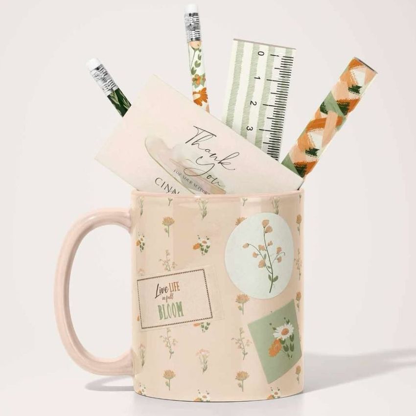 Mug mockup featuring a pastel ceramic mug with floral designs, filled with pencils, a ruler, and stationery on a light background.