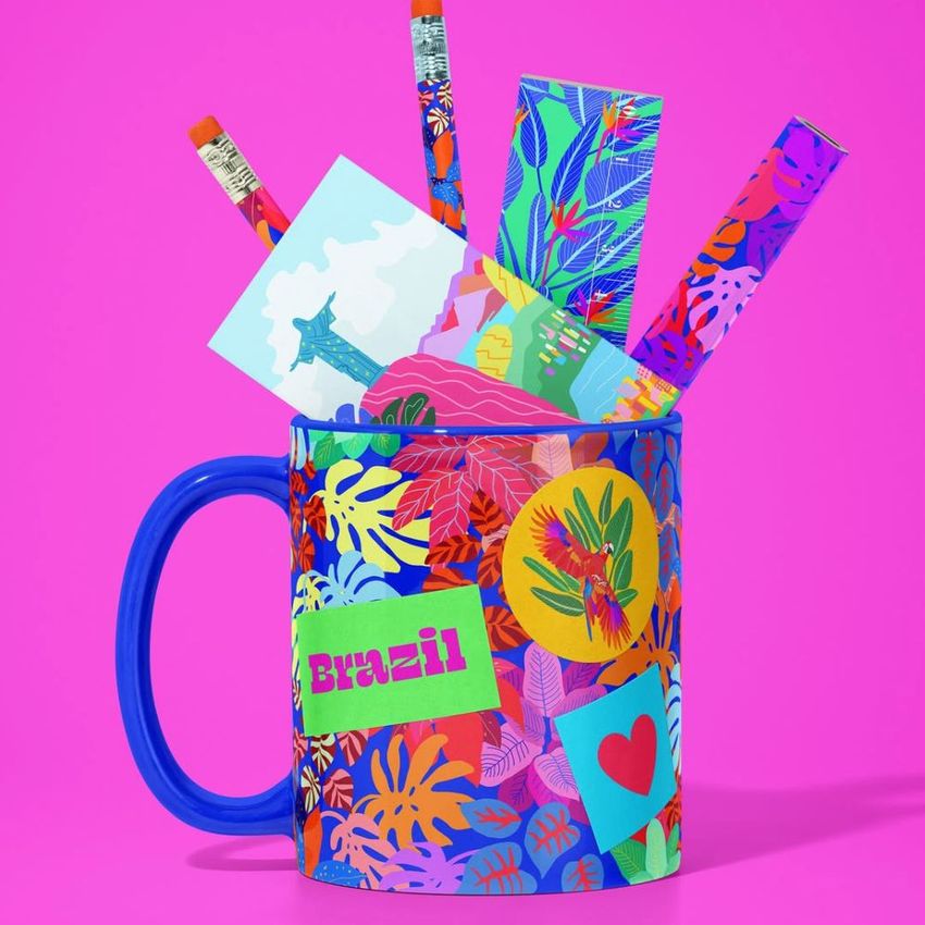 Colorful mug mockup decorated with tropical leaf patterns, filled with pencils, cards, and bookmarks on a bright pink background.