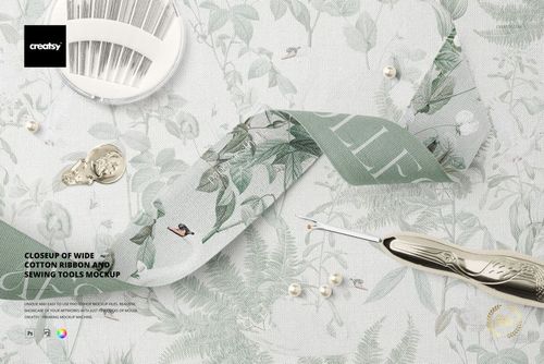 Wide cotton ribbon featuring leafy design, sewing needle, buttons, and pearls arranged on patterned fabric in a mockup.