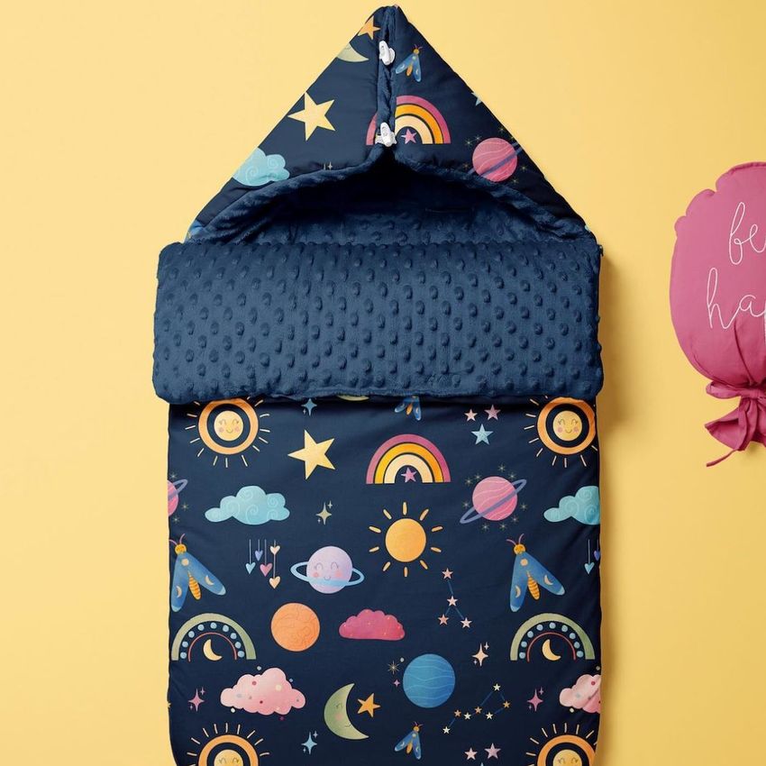 Baby sleeping bag mockup with a navy blue background, decorated with colorful suns, clouds, rainbows, and stars, shown on a yellow surface.