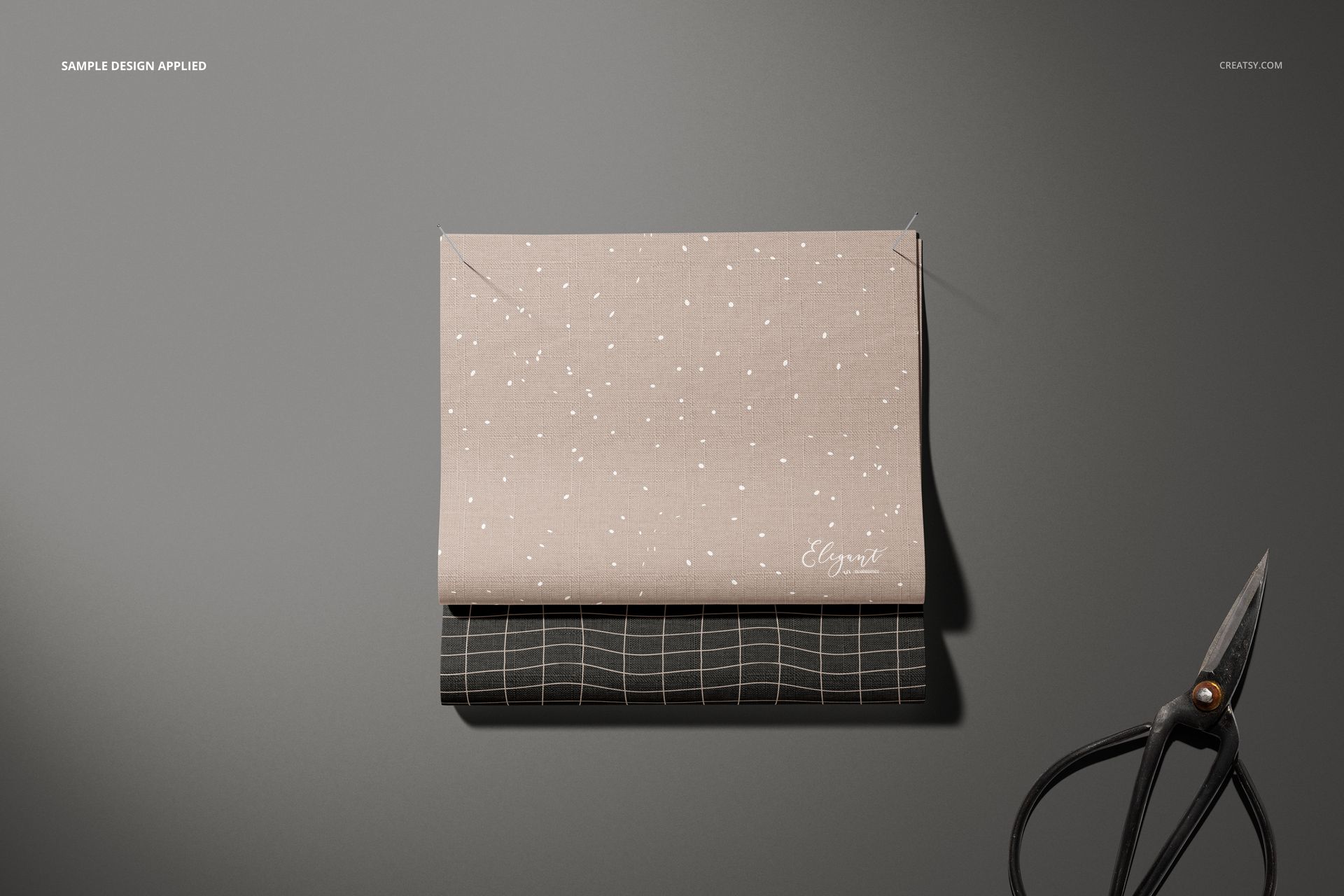 Fabric swatches mockup showing a beige dotted fabric layered over a black grid fabric, scissors placed beside them.