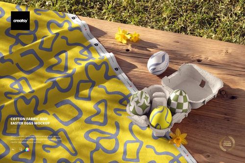 PSD mockup showing cotton fabric with blue geometric shapes and Easter eggs in a carton, set on wood with yellow flowers.