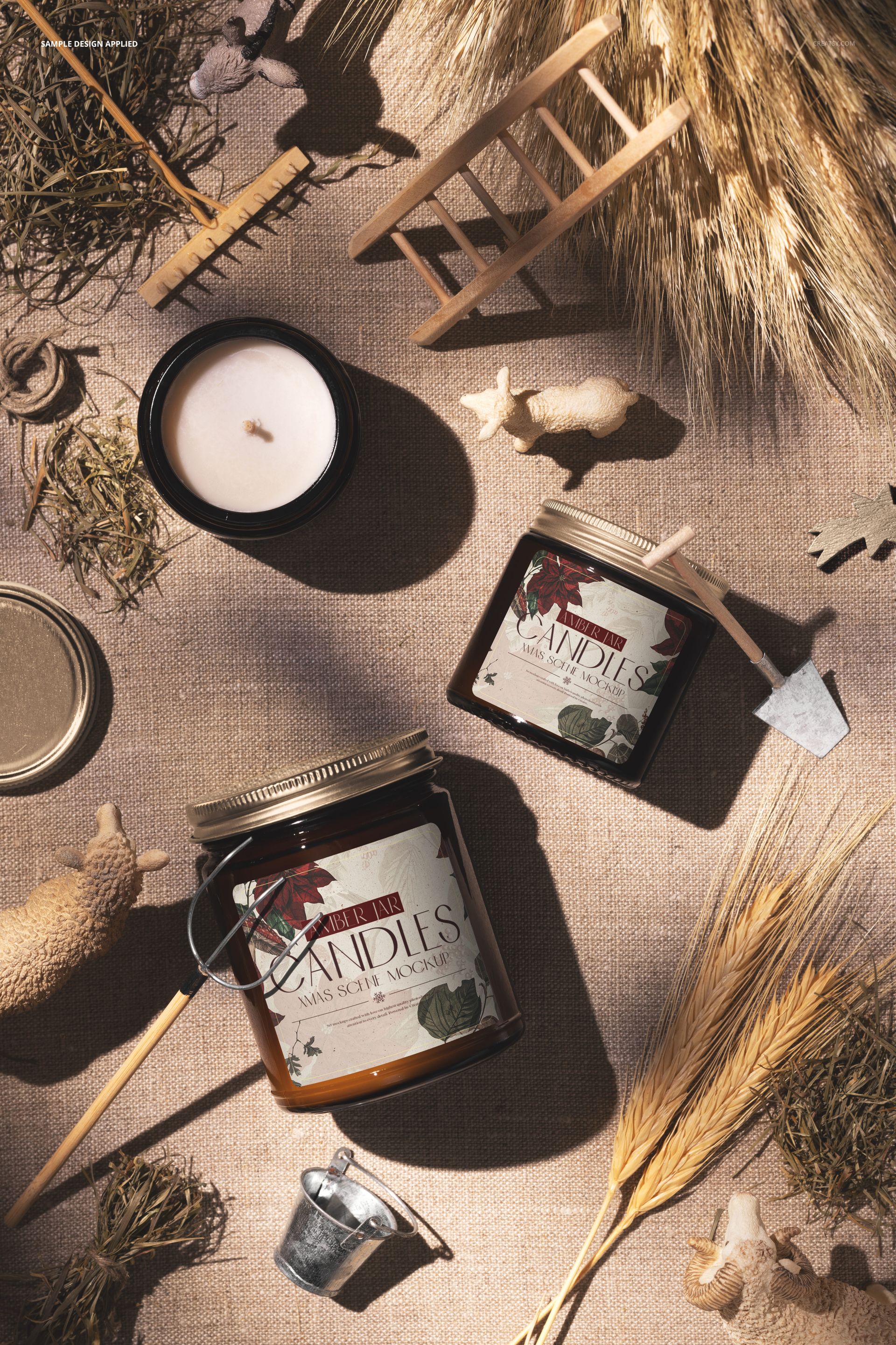 Amber jar candle PSD mockup displayed on textured fabric with dried wheat, straw, and miniature farm-themed props.