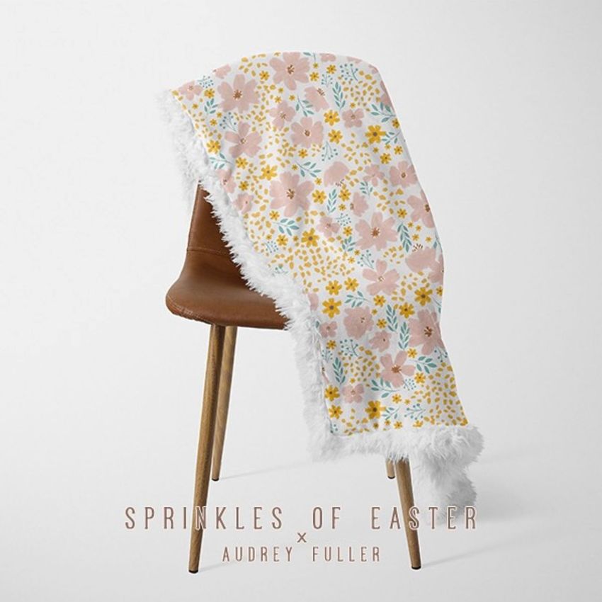 Sherpa baby blanket mockup draped over a brown chair, featuring a pastel floral pattern and fluffy white edges on a plain background.