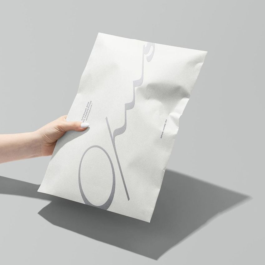 Hand holding a white kraft mailer mockup with minimalist gray text design, set against a plain light gray background.