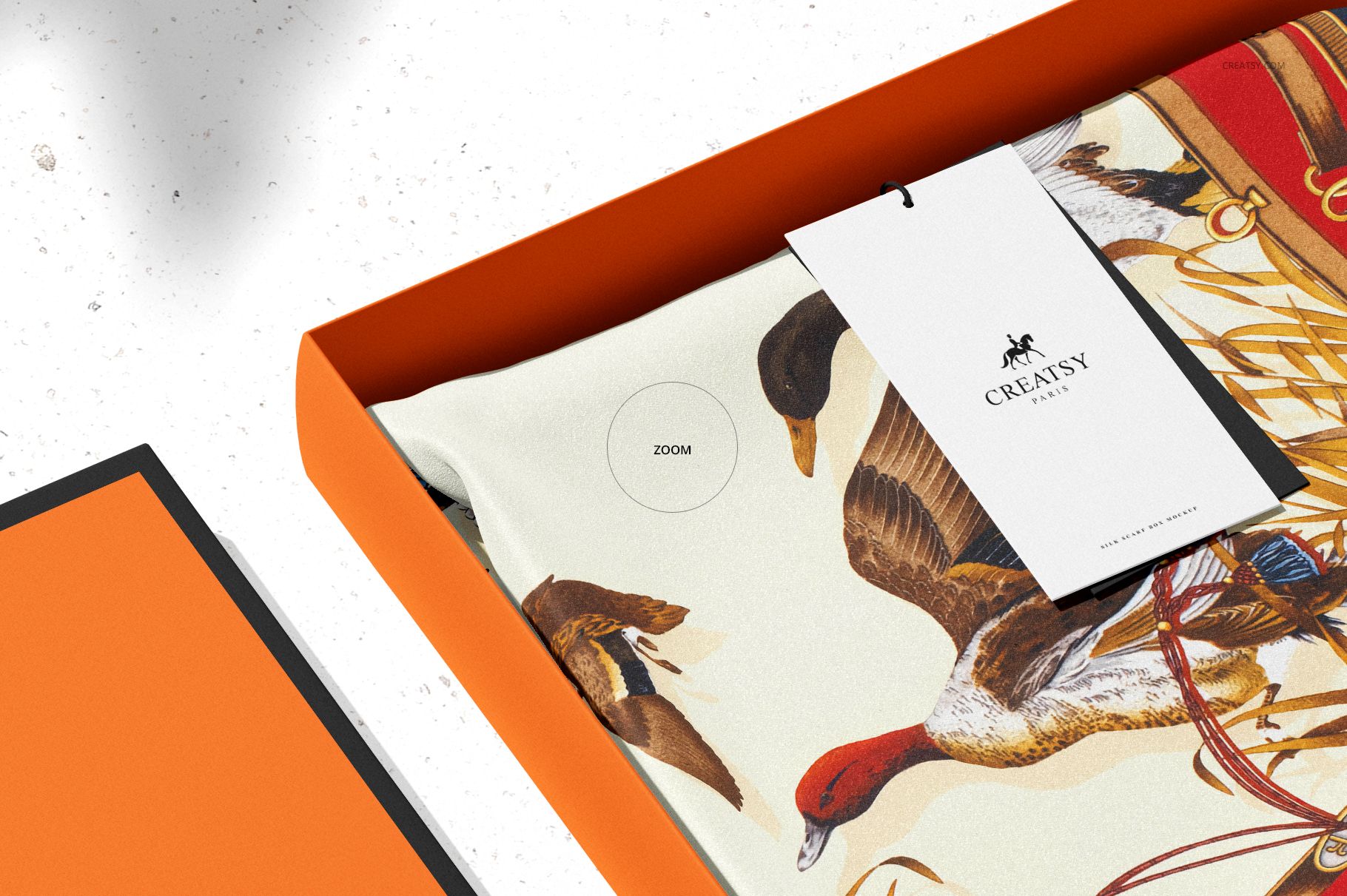 Silk scarf box mockup showing an orange rectangular box with a patterned scarf and a branded tag inside.