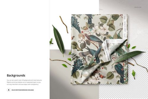 PSD mockup showing folded fabric with floral and bird pattern, viewed from above with scattered leaves and textured backgrounds.