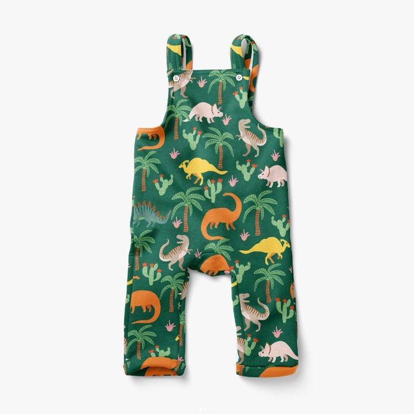 Kids fleece dungarees mockup featuring a green fabric with colorful dinosaur and palm tree illustrations on a white background.