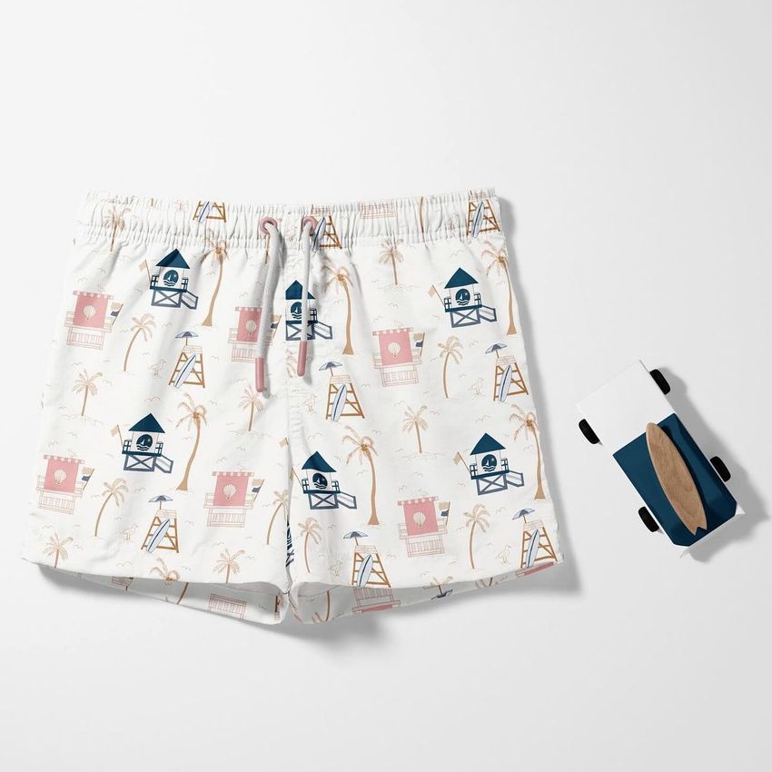 Kids swim shorts mockup featuring a lifeguard tower and palm tree pattern in pastel colors, shown on a white background with a wooden toy car.