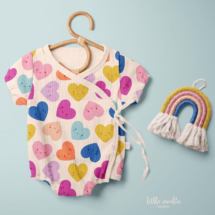 Muslin onesie mockup featuring a colorful heart pattern on a cream background, displayed on a wooden hanger against a light blue surface.
