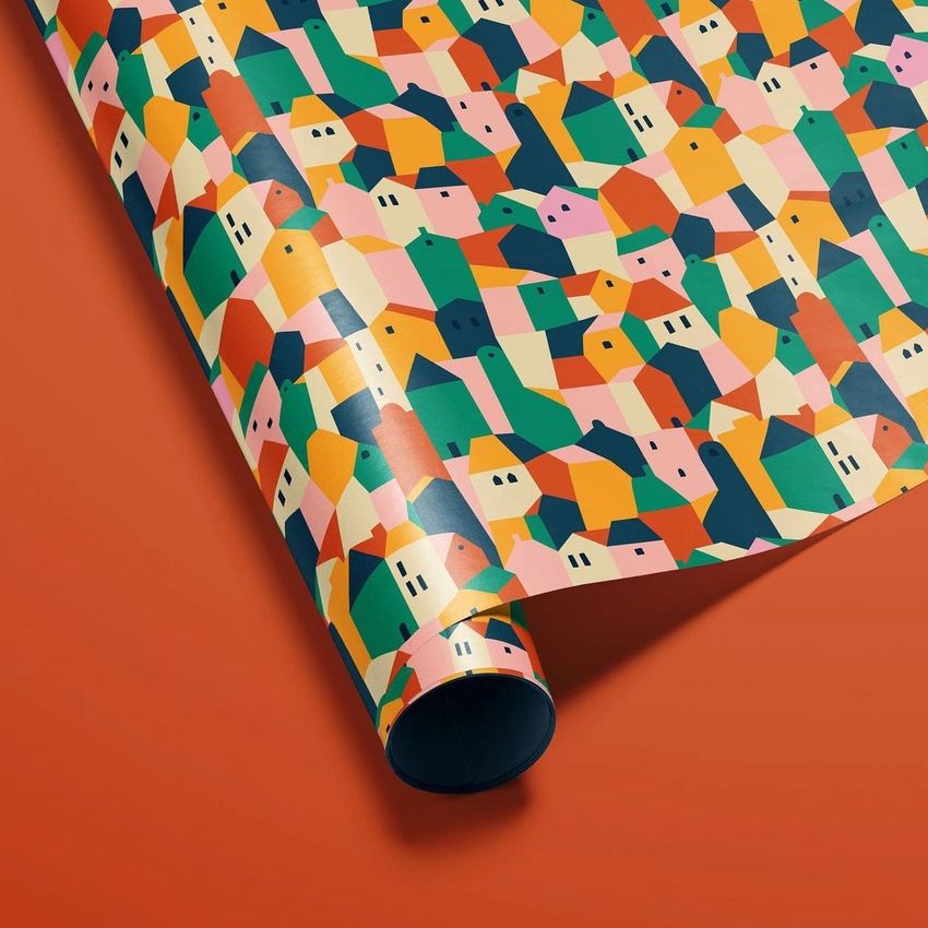 Gift wrapping paper mockup featuring a roll with a colorful geometric house pattern on a solid orange background.