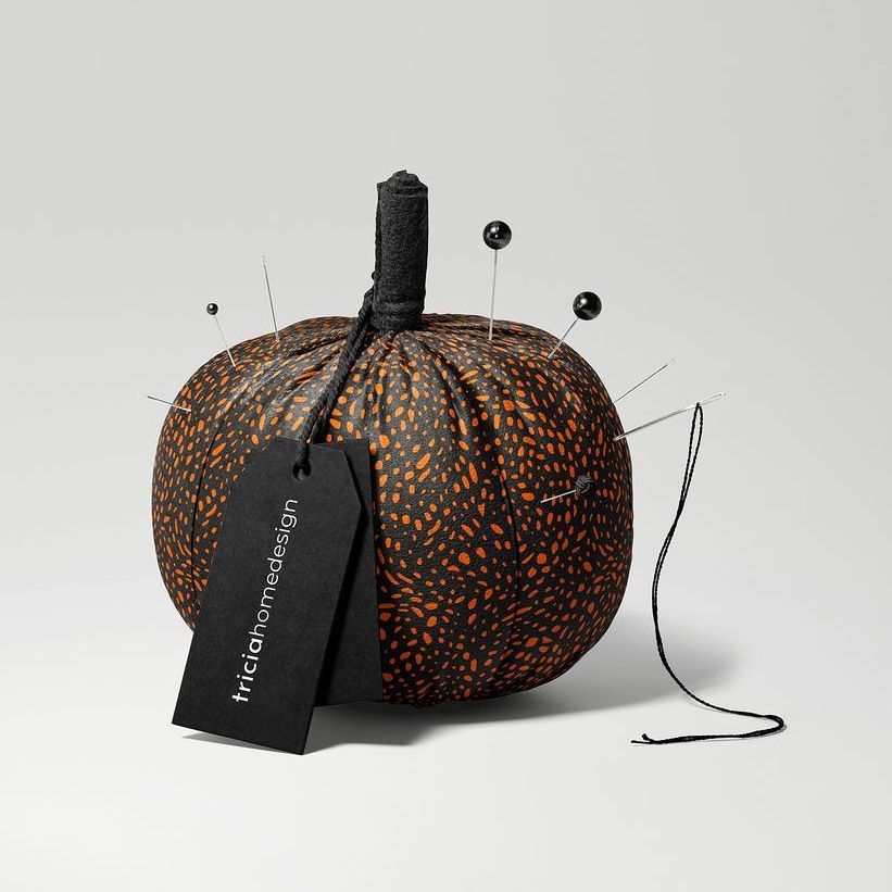 Fabric pumpkin mockup with orange and black dotted pattern, used as a pincushion with black and silver pins and a black tag.