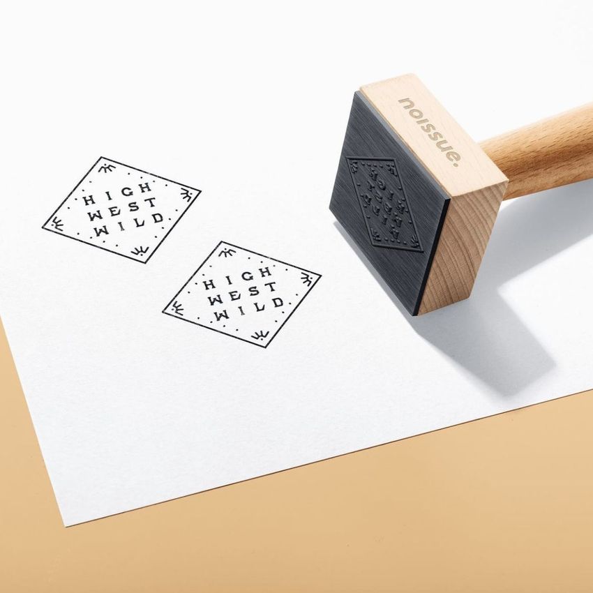 Wooden stamp mockup on a white sheet with two stamped diamond-shaped logos and a light beige background.