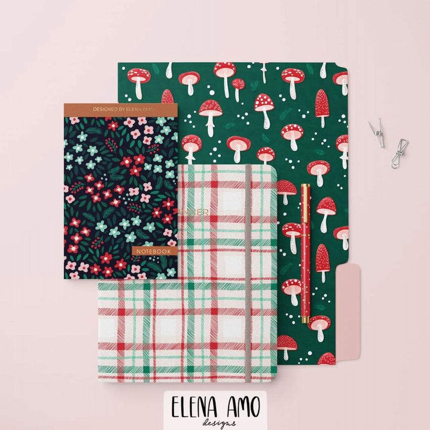 Stationery set mockup featuring a green mushroom-patterned folder, floral and plaid notebooks, a red pencil, and paper clips on a pale pink background.