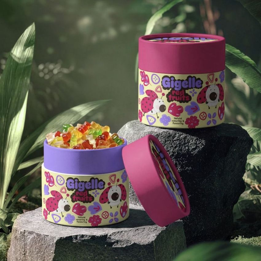 Paper tube packaging mockup featuring colorful jungle-themed designs and gummy candies, set on rocks among green foliage outdoors.