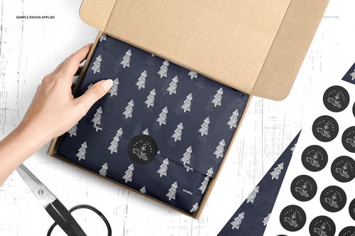 Open mailer box with navy blue wrapping tissue paper featuring white tree patterns, viewed from above on a white surface.