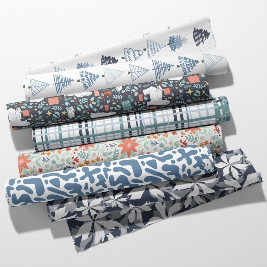 Fabric rolls mockup featuring six rolls with winter and botanical patterns in blue, white, and green tones on a light surface.