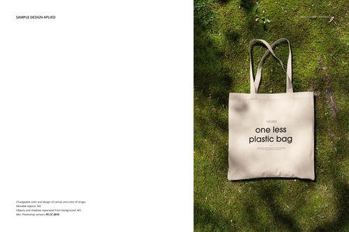 Beige tote bag mockup with long handles, placed on green grass, front view showing printed text design.