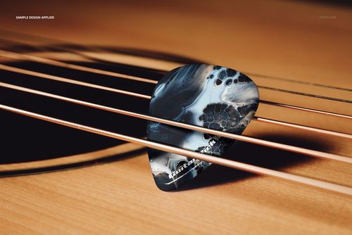 Guitar pick featuring a marbled black and gray design placed across the strings of a wooden acoustic guitar in a mockup scene.
