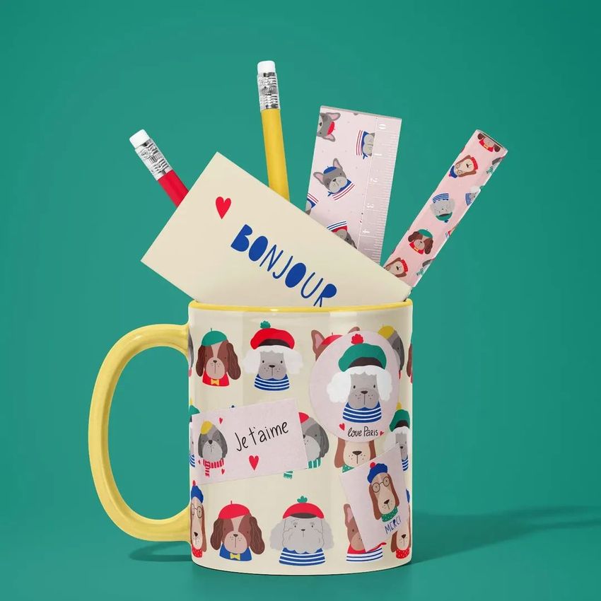 Mug mockup with a yellow handle featuring illustrated French-style dogs, filled with stationery items like pencils, a ruler, and cards on a green background.