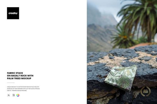 PSD mockup showing folded fabric with leafy design on a textured rock surface, surrounded by lush palm trees.