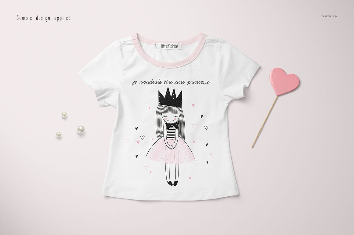 Front view of a girls T-shirt mockup with a cartoon princess design, white fabric, pink collar, and decorative props.